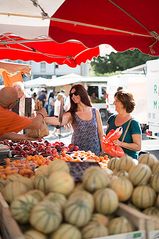 Une femme aux cheveux longs récupère un sac de fruits que lui tend le marchand.