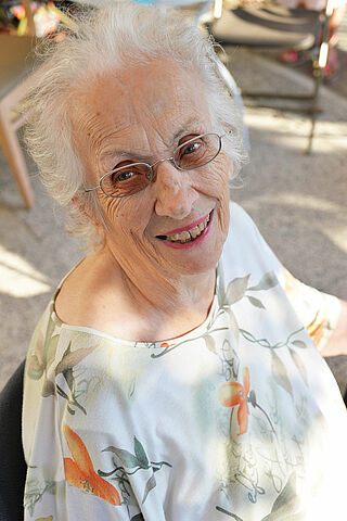 Femme âgée aux cheveux blancs portants des lunettes et souriant.