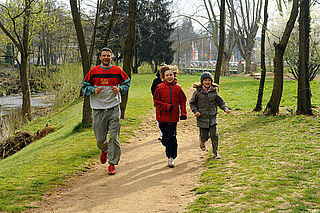 Un adulte et deux enfants, souriants, courant dans une allée du parc.
